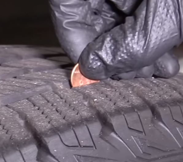 Man judging tire pressure by inserting coin in tread spaces